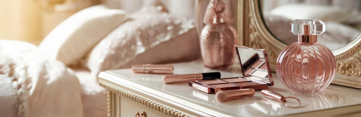 A vanity table with rose gold makeup brushes, eyeshadow palette, lipstick, and a perfume bottle reflects a love for beauty and self-care. A mirror and soft, decorative pillows in the background create an elegant, feminine atmosphere.